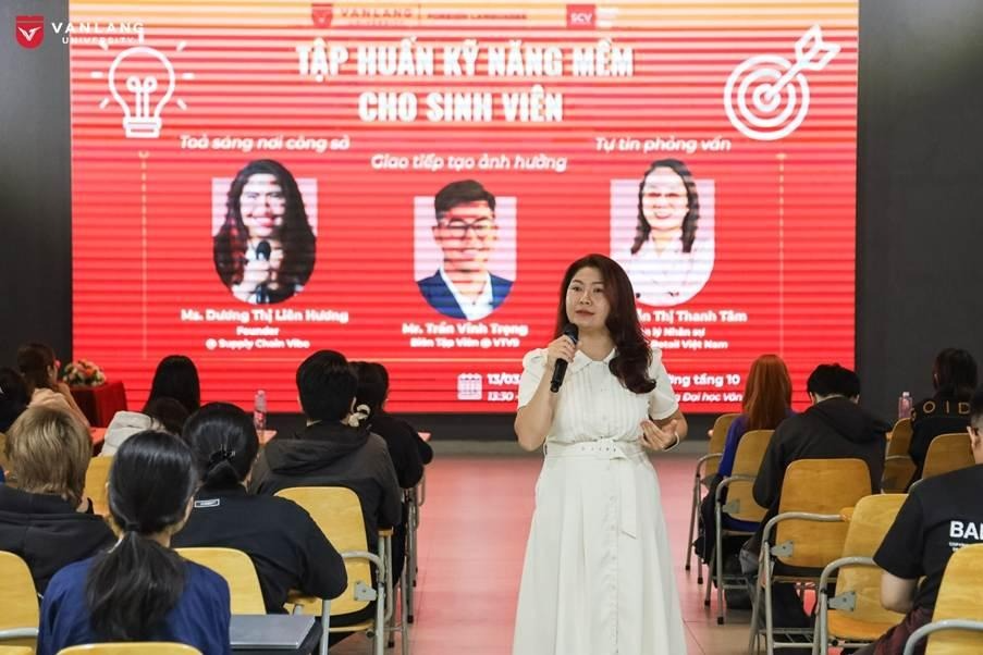 A person in a white dress holding a microphone in front of a large screen

Description automatically generated